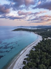 Aerial view of a beach and coastal forest with a peaceful sea at sunset. Aerial view of Glarokavos