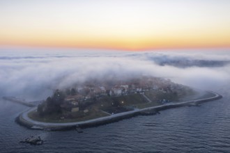 An island surrounded by mist at sunrise with calm waters. Aerial view to thick fog descends over