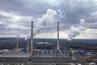 Aerial view of a large power plant with smokestacks emitting smoke into a cloudy sky. Aerial view