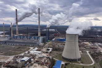 Aerial view of a power plant with multiple smokestacks releasing smoke under a cloudy sky. Aerial