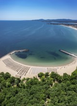 Scenic beach with lined umbrellas beside lush greenery and an expansive ocean. Aerial view to