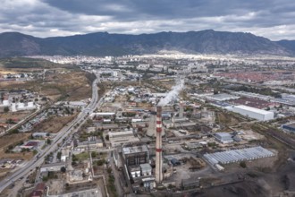 City with industrial facilities and smokestacks nestled among nearby mountains. Aerial view of