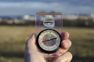 Male hand holding glass compass, nature in background, sunny autumn day, life change and new years