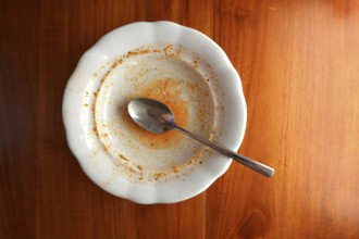 Empty white plate with spoon on wooden table, flat lay top view, red leftovers from soup or sauce