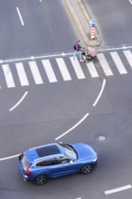 Blue car heading to pedestrian crossing with unrecognizable young woman pushing baby carriage,