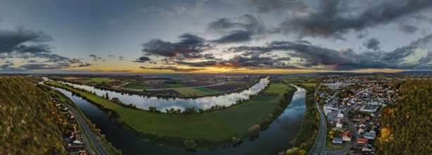The landscape shows a picturesque sunset over a river. A city is visible in the foreground,