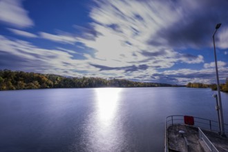 A quiet river stretches under a cloudy sky. The clouds move gently while the sunlight makes the