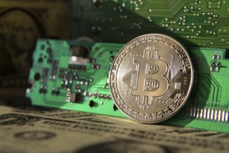 Silver bitcoin coin with dollars and computer motherboard, cryptocurrency mining and investing