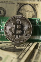 Silver bitcoin coin with dollars and computer motherboard, cryptocurrency mining and investing