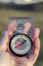 Male hand holding glass compass, nature in background, sunny autumn day, life change and new years