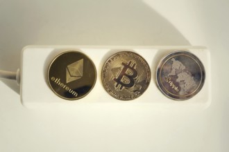 Bitcoin, Ethereum and Ripple coins lying on power strip extension cord with 3 sockets, largest