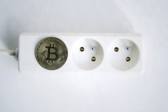 Bitcoin coin lying on power strip extension cord with two empty sockets, cryptocurrency investing,