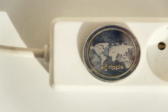 Ripple coin lying on power strip extension cord with empty socket, cryptocurrency investing, energy