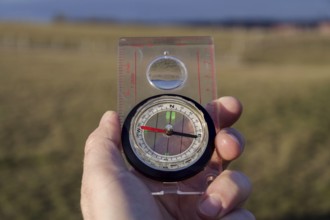 Male hand holding glass compass, nature in background, sunny autumn day, life change and new years
