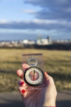 Female hand holding glass compass, nature in background, sunny autumn day, life change and new