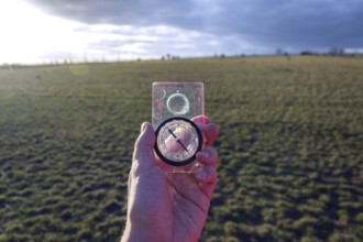 Male hand holding glass compass, nature in background, sunny autumn day, life change and new years
