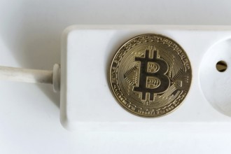 Bitcoin coin lying on power strip extension cord with empty socket, cryptocurrency investing,