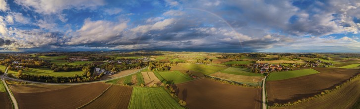A vast landscape with green meadows, fields and a clear sky. A rainbow stretches across the hilly
