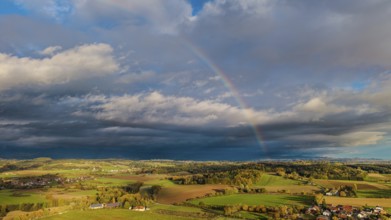 A rainbow stretches across the vast fields and villages. The scene shows vivid colors under a