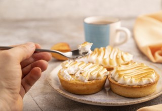 French lemon tart with meringue with hand on brown concrete background, cup of coffee, orange linen