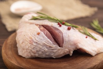 Raw Turkey Thigh with spices and rosemary on cutting board on brown wooden background and linen