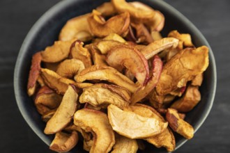 Dried Apples in ceramic bowl on black wooden background. Side view, close up. healthy food,