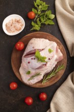 Raw Turkey Thigh with spices and rosemary on cutting board on black concrete background and linen