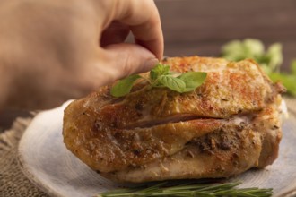 Fried Turkey Thigh with spices and rosemary on plate with hand on brown wooden background and linen