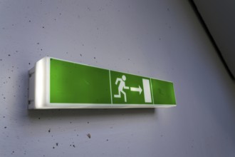 Green shining escape exit sign on white concrete wall