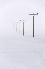 Electricity pylons from distribution power station disappearing in deep fog, winter freezing