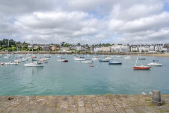 The view from a stone harbor wall shows numerous sailing and motor boats on the turquoise water of