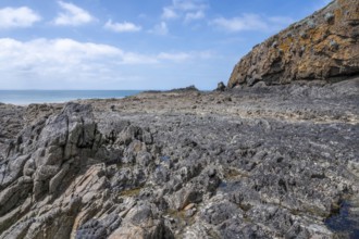An extensive, humid sandy and rocky beach is exposed in a wide bay at low tide (low tide), with wet