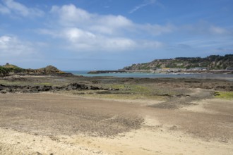 An extensive, humid sandy and rocky beach at low tide stretches out in the foreground, while in the