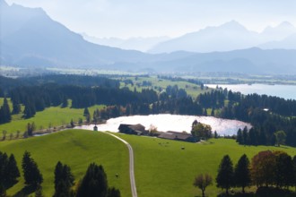 Panorama with green hills, Hegratsrieder See, wooded areas and mountains in the background, farm,