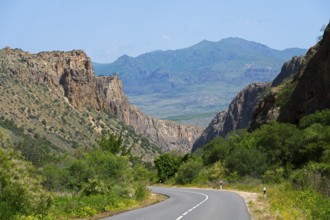 Road curves through a wide valley with mountain ranges in the background, picturesque road leading