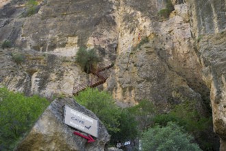 Steep rock wall with a cave and a signpost, Amaghu Gorge, rock wall has a cave with bats to which