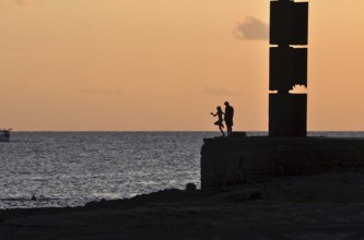 Silhouette of a girl jumping into the sea while a boy is watching, Majorca, balearics, spain