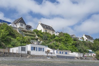 A series of colorful, historic beach cabins with walls of natural stone line the rocky beach at the