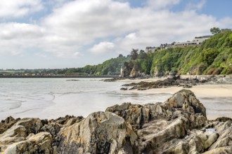 Sharp-edged rocks and sandy beach line Anse aux Moines with its densely overgrown cliff and houses