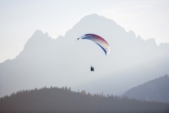 Paragliders in the mountains in morning light with foggy, calming atmosphere, Schwangau, Ostallgäu,