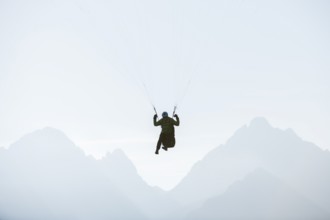 A paraglider floats against a mountain backdrop in morning light, Schwangau, Kostallgäu, Allgäu,