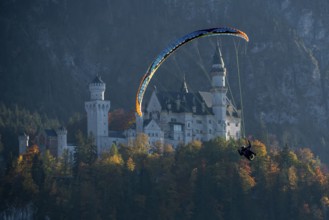 Paragliders in front of Neuschwanstein Castle, surrounded by autumn forests and mountains,