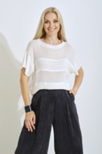A model is wearing a stylish white top with horizontal stripes and dark, wide-legged pants. She