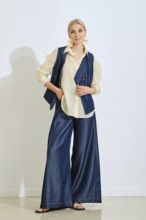 A model showcases a fashionable outfit with a denim vest and wide-leg pants paired with a light