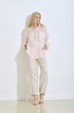 A model stands confidently in a light pink button-up shirt and beige pants. She poses with hands in