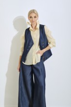A confident woman showcases a chic fashion look featuring wide denim pants and a fitted vest over a