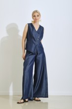 A woman models a fashionable navy vest and wide-leg pants in a contemporary studio. Natural light