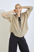 A woman strikes a confident pose while wearing a chic beige shirt complemented by bold accessories.