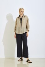 A model stands confidently in a bright studio space wearing a stylish beige top and black wide-leg