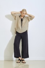 A model showcases a relaxed outfit consisting of a loose beige shirt and dark wide-leg pants